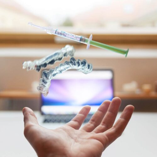 Invisalign Services in Randolph, NJ 5 Whitening trays and syringe floating above hand